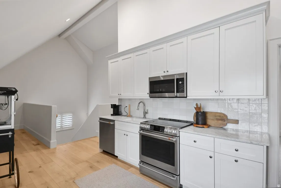 White shaker cabinetry with stainless steel appliances, light-toned wood-finish flooring, and a white subway tile backsplash