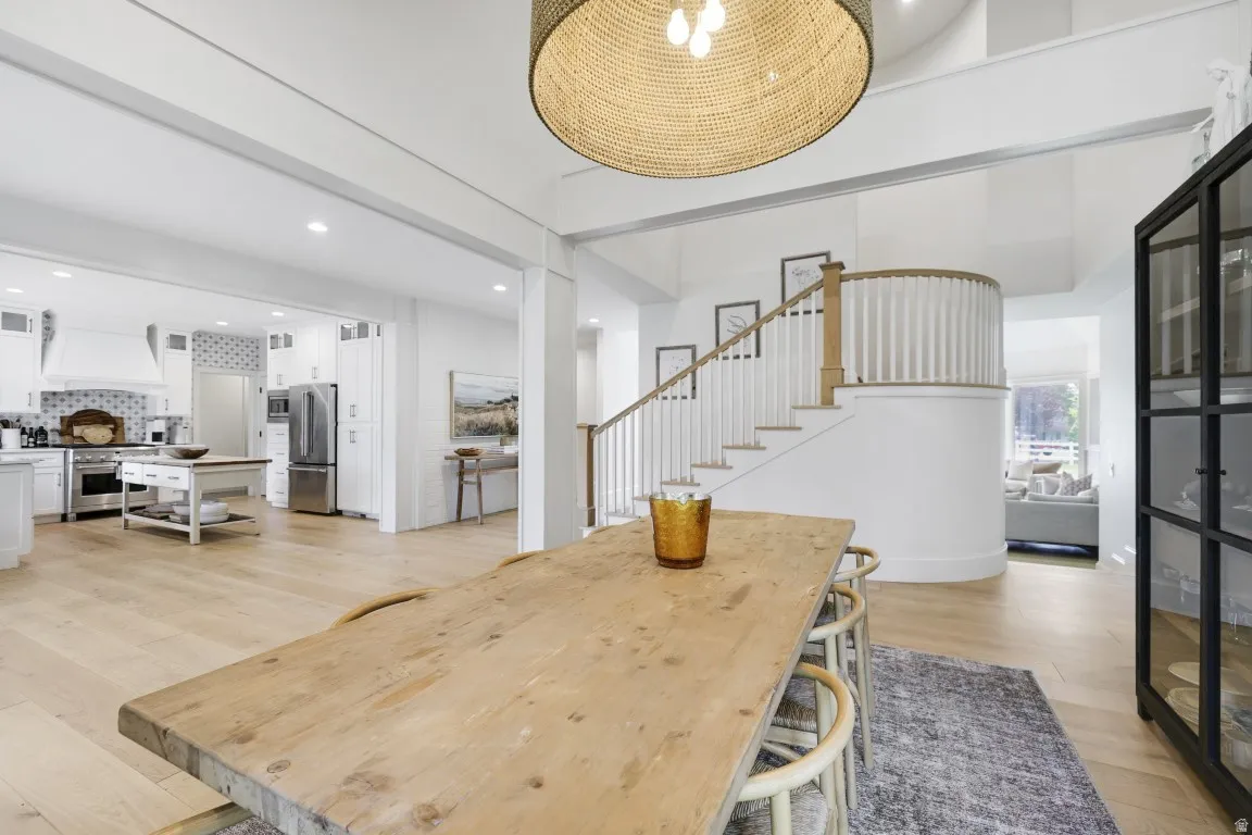 Open-concept kitchen and dining area featuring light wood-finish flooring, a white kitchen with stainless steel appliances, and a curved staircase with wood and white balusters