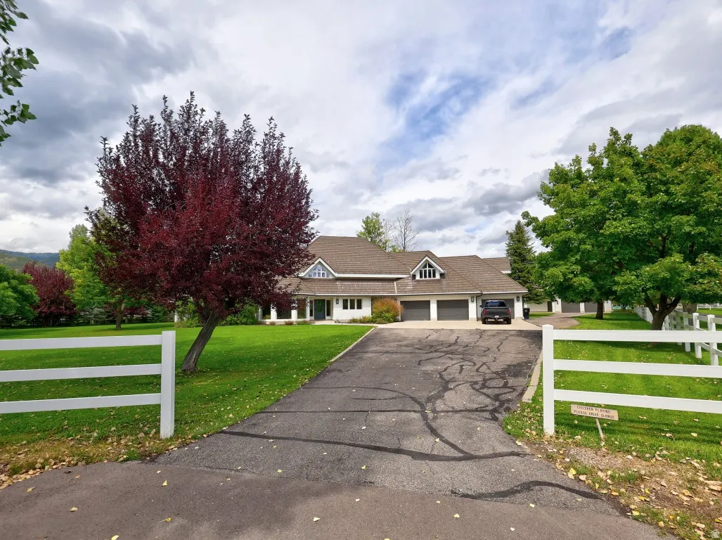 Gabled roofline residence featuring a three-car garage, white picket fence, and a paved driveway