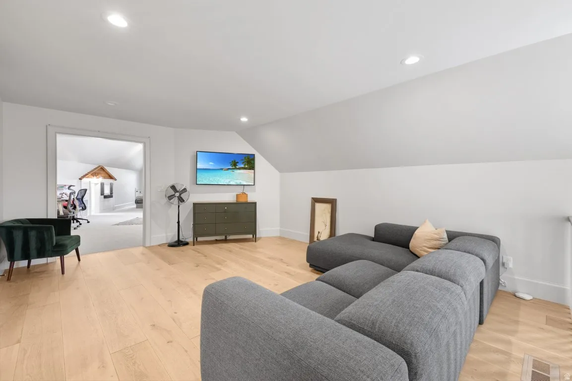 Bright attic space featuring light wood-finish flooring, recessed lighting, and a white painted vaulted ceiling