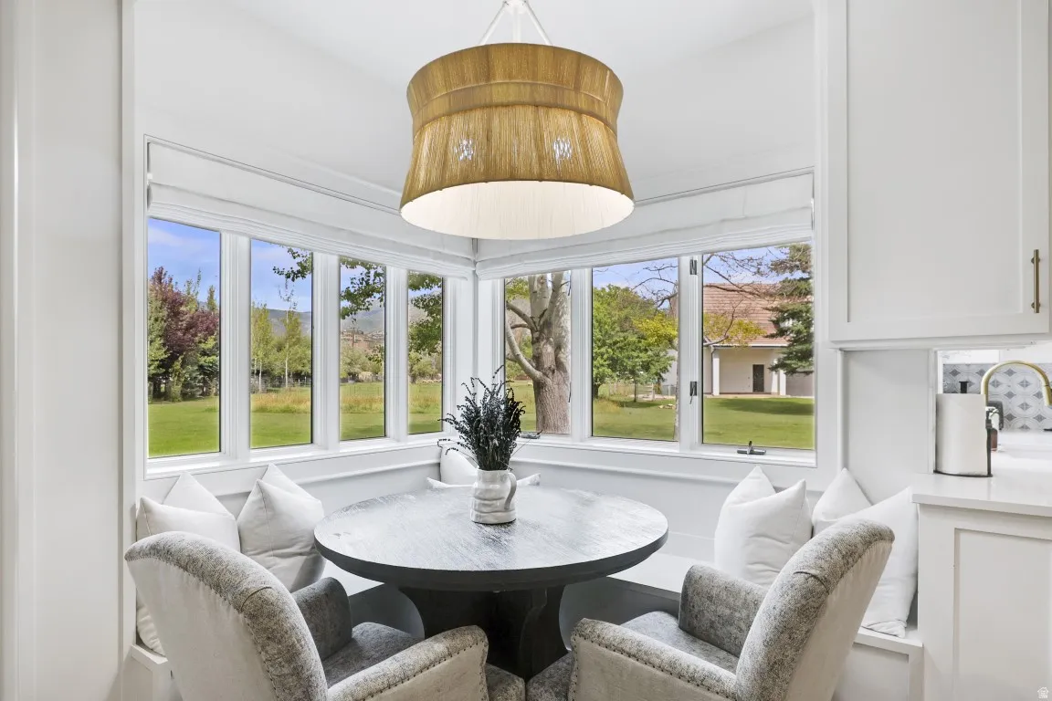Built-in banquette seating with storage, corner window placement, suspended light fixture, white cabinetry, and a countertop with an integrated sink