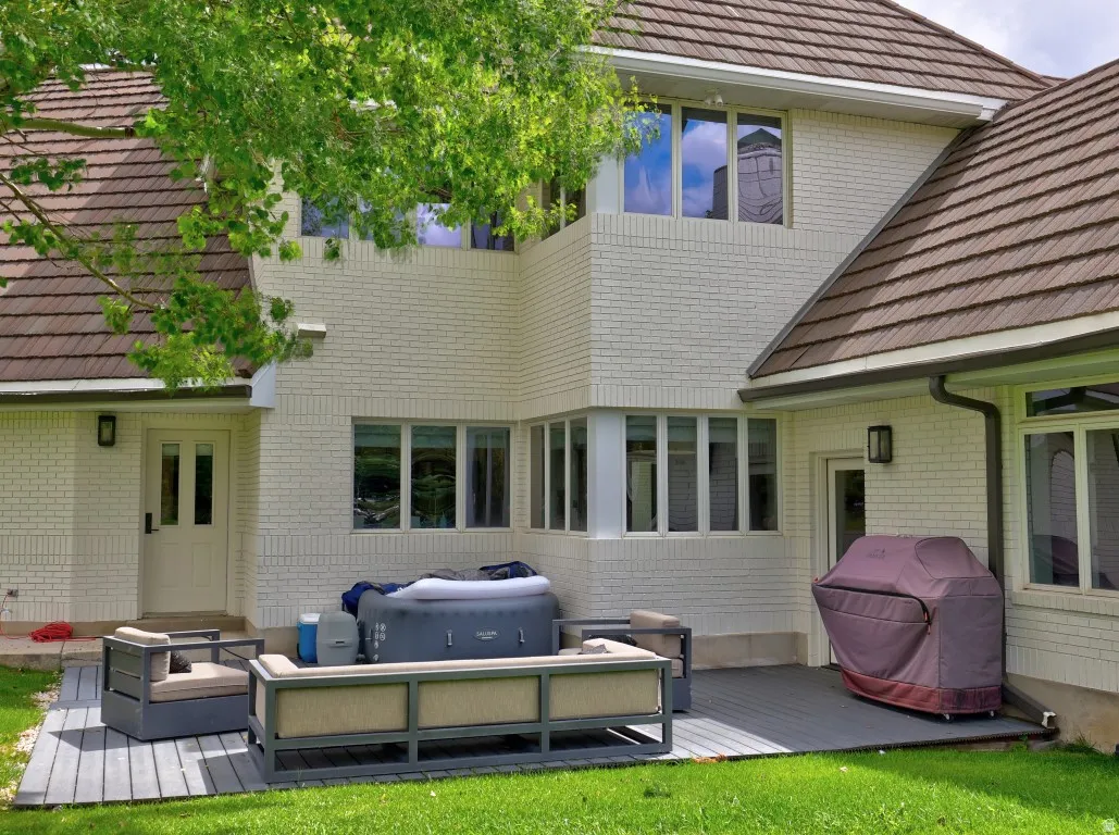 Textured tile roof, white brick exterior, multiple window configurations, dark gray composite decking, and exterior light fixtures