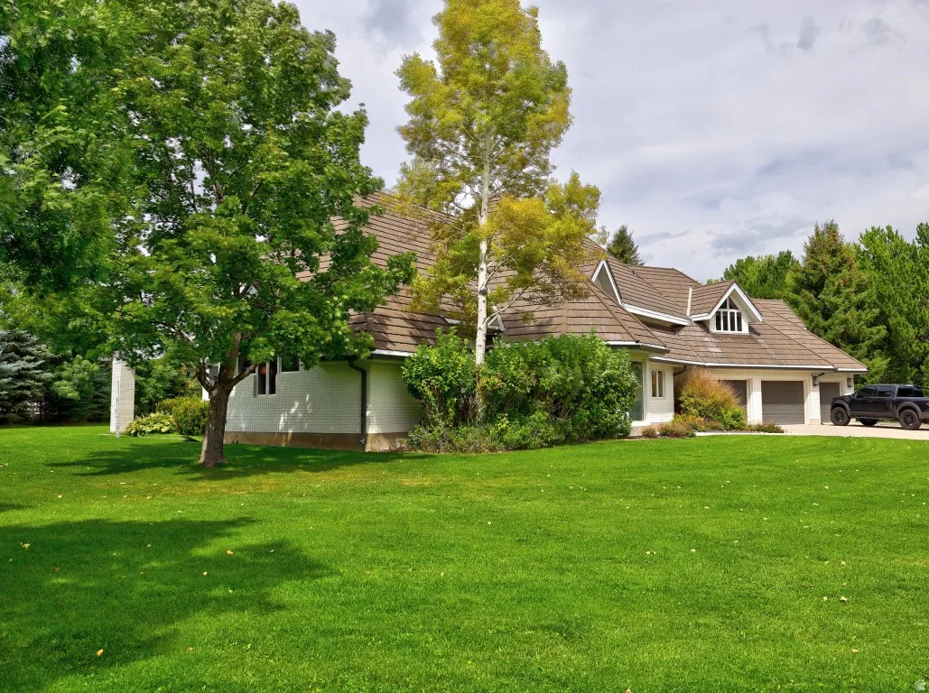 Expansive lawn with mature trees, a multi-car garage, and dormer windows on a gabled roof