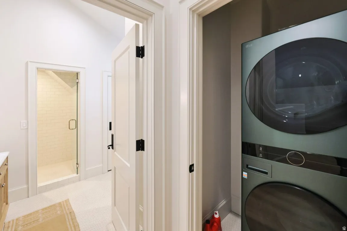 Stacked laundry appliances, frameless glass shower enclosure, subway tile shower surround, and a vaulted ceiling