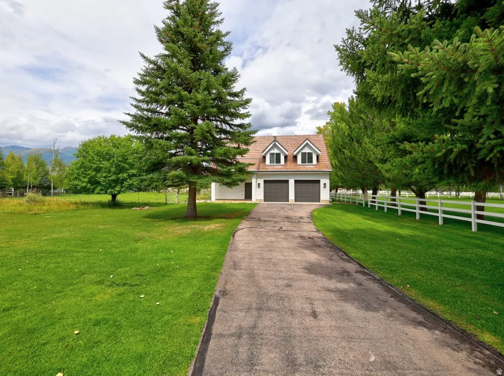 Expansive green lawn with mature trees, a paved driveway, and a white picket fence