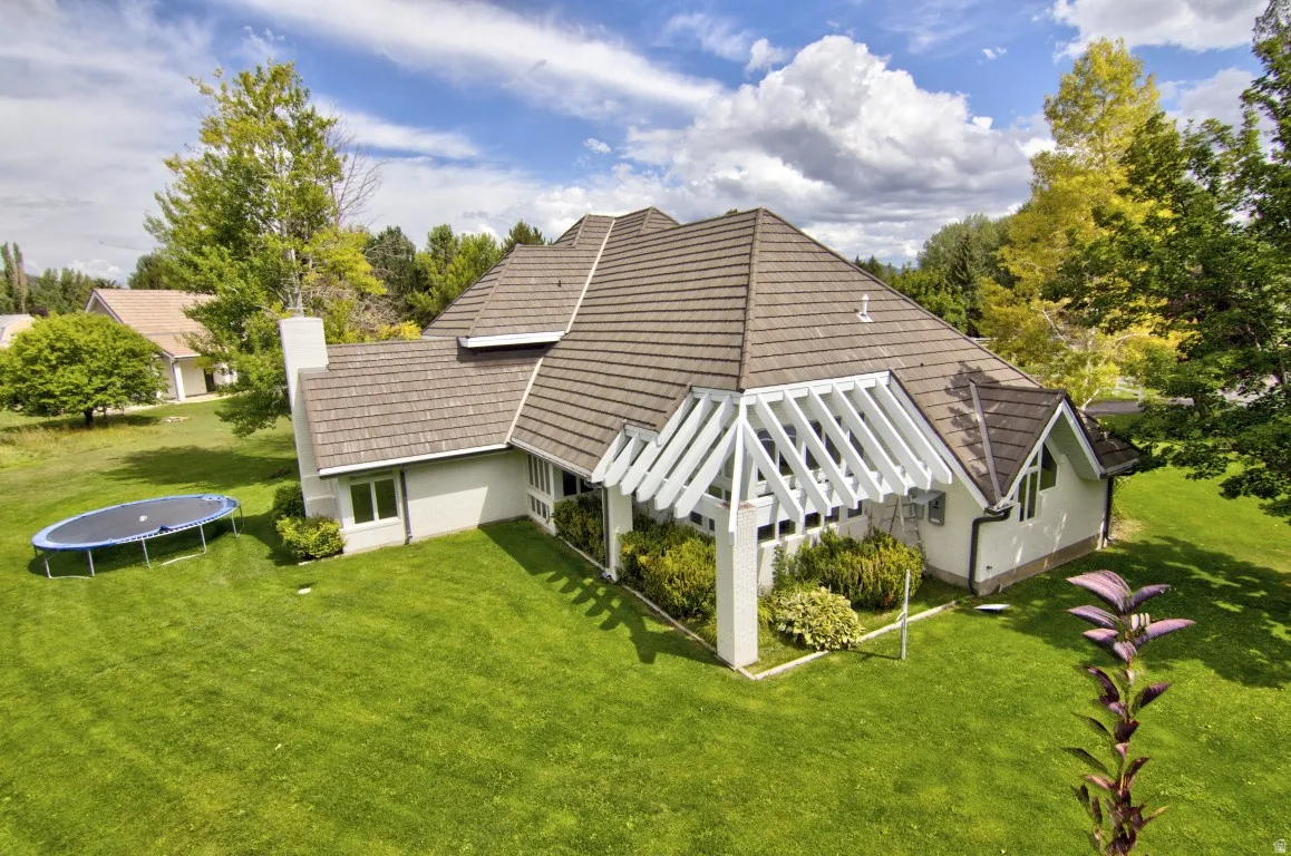 Pitched roof with dimensional shingles, white stucco exterior, prominent chimney, architectural pergola, and established landscaping