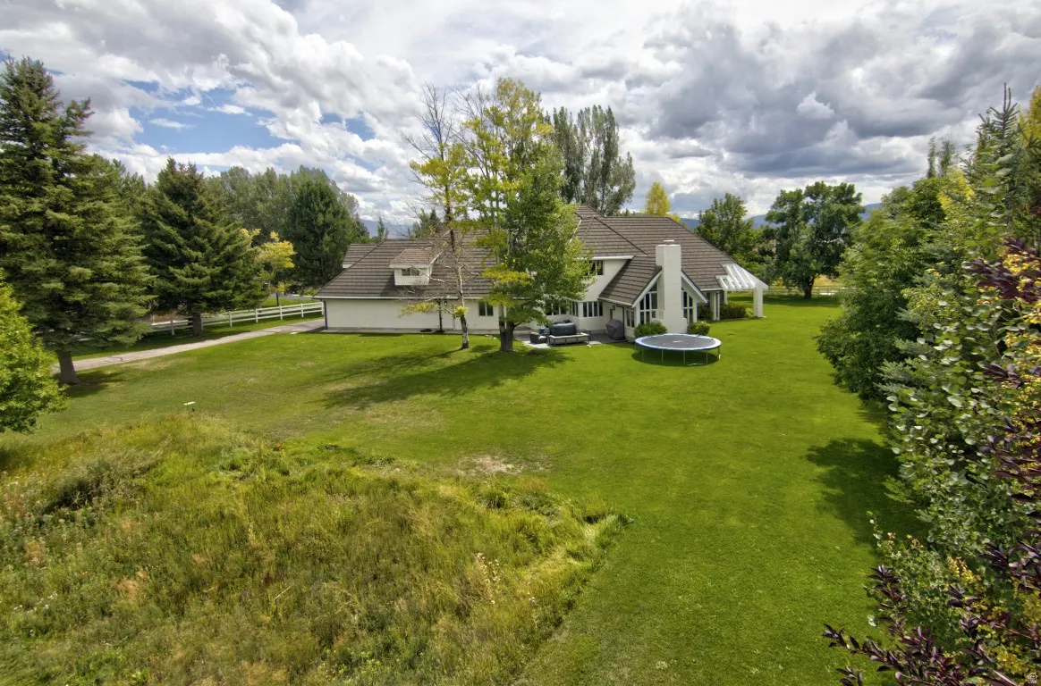 Expansive lawn with mature trees, a white picket fence, and a covered patio structure