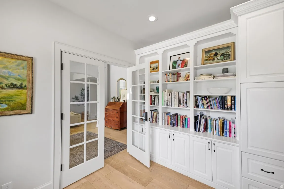 Built-in shelving with crown molding, white cabinetry with black hardware, wood-finish flooring, and French doors