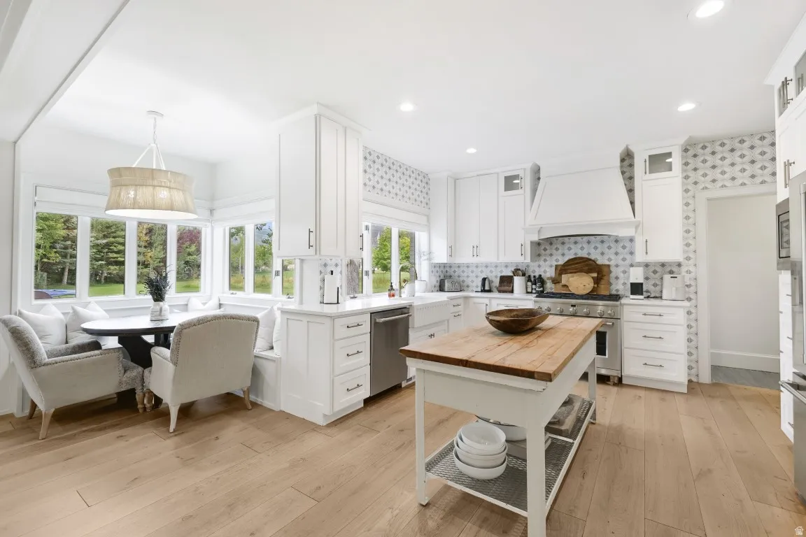 White cabinetry, wood-finish flooring, stainless steel appliances, patterned backsplash, and an integrated dining nook