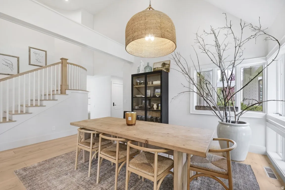 Vaulted ceiling with an oversized woven pendant light, light wood-finish flooring, white walls, and a staircase with white balusters and wood handrails