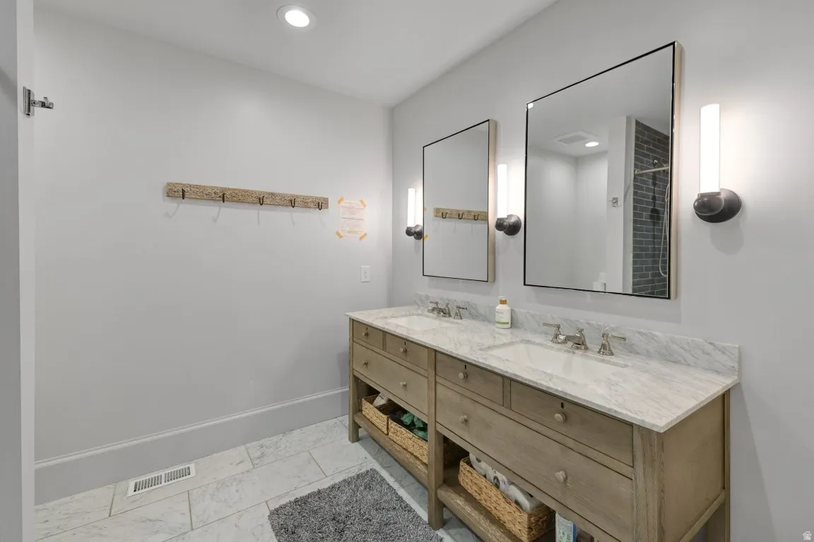 Dual sink vanity with stone countertop, individual framed mirrors, and wall-mounted sconce lighting