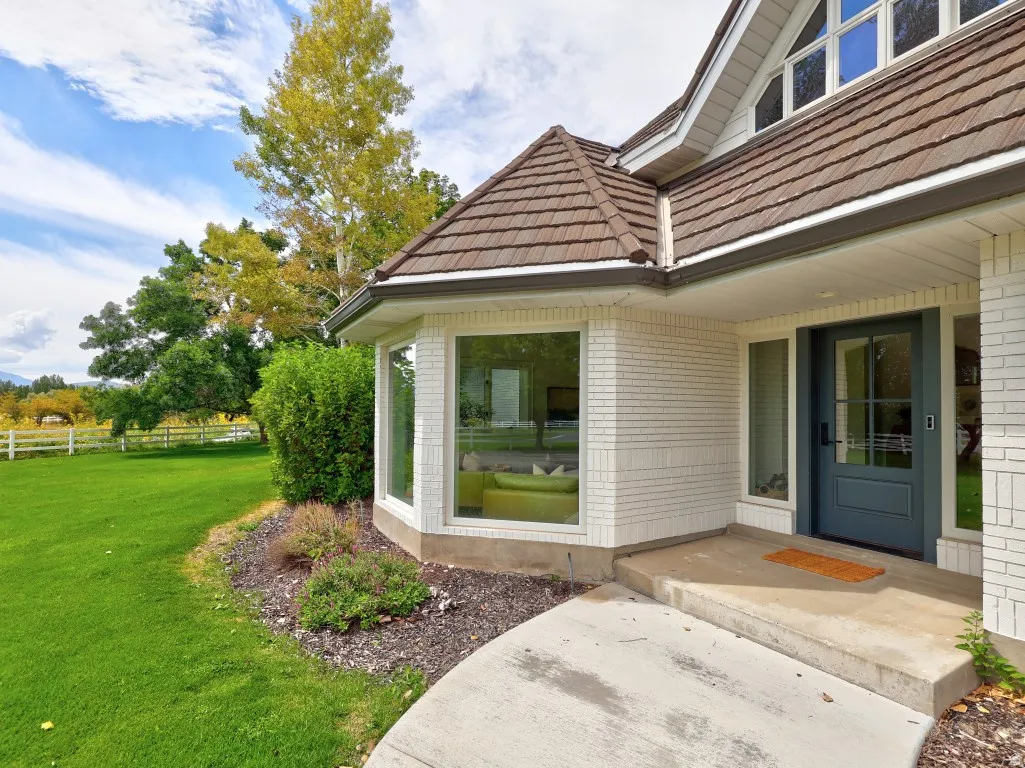 Elegant brick exterior with white trim and cedar shake roofing, featuring a curved bay window section with expansive glass panels, dark entry door, and concrete walkway