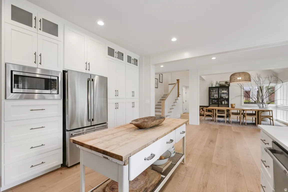 Chef's kitchen featuring white cabinetry with brushed nickel hardware, stainless steel appliances including a built-in microwave and refrigerator, a wood-top island with storage drawers, and wood-finish flooring throughout