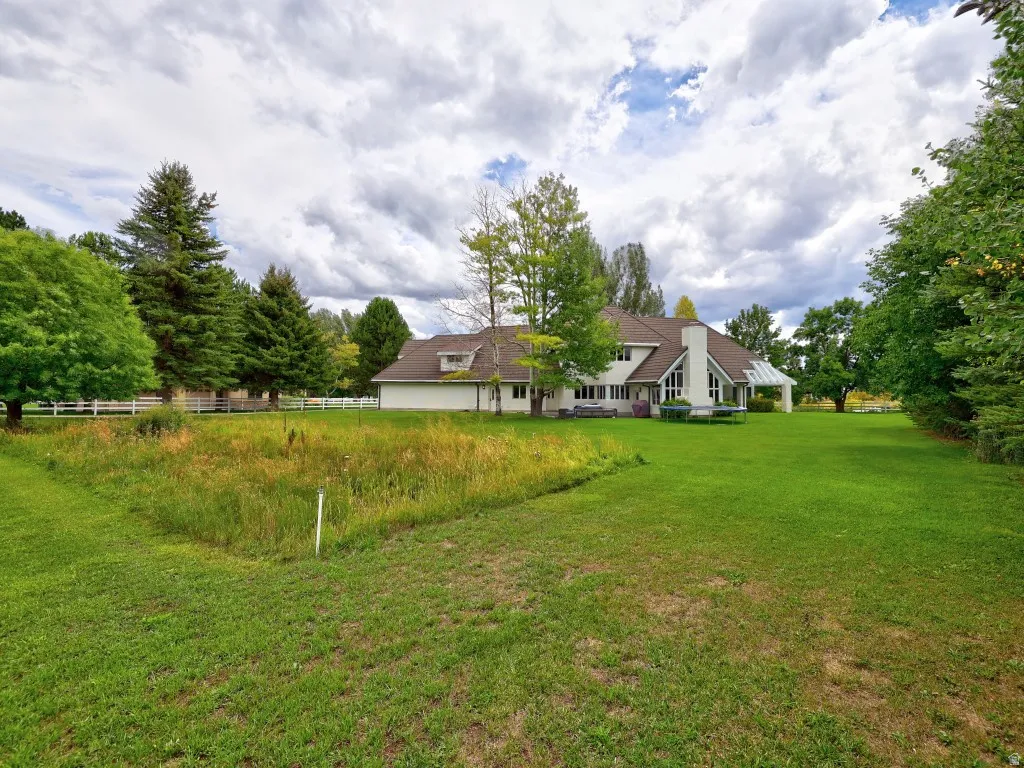 Expansive rear yard with a manicured lawn, mature trees, and a white picket fence bordering a natural area
