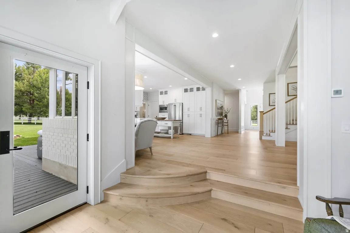 Hardwood flooring, crisp white walls, recessed lighting, white kitchen cabinetry, and stainless steel appliances
