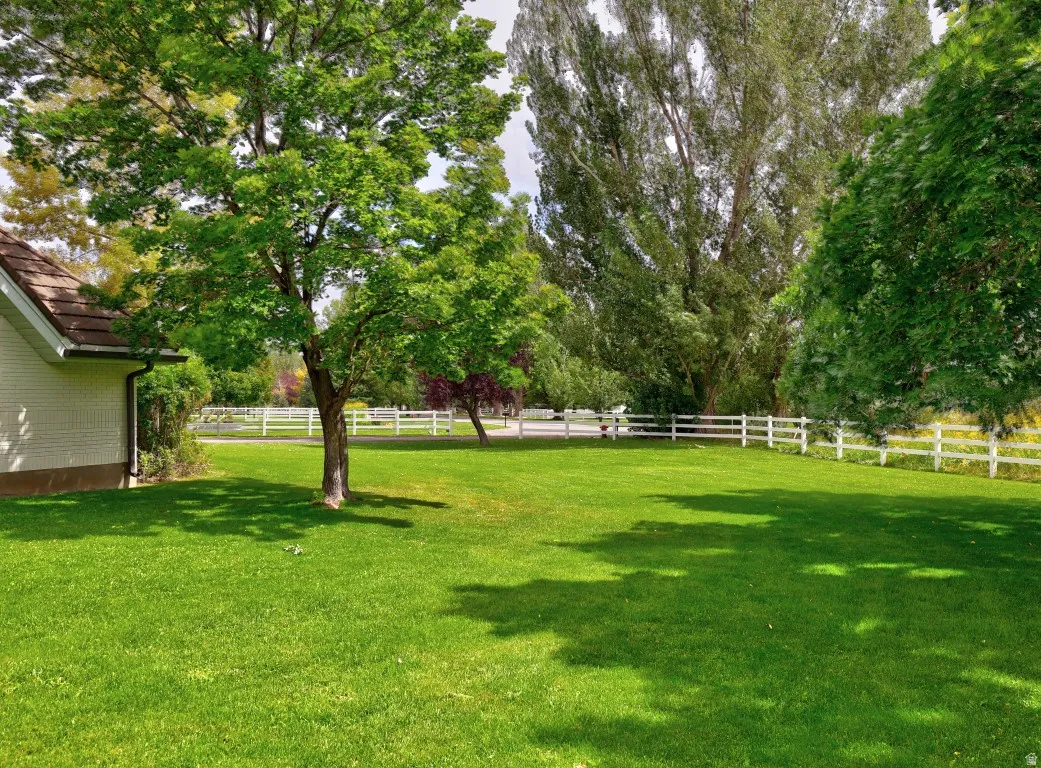 Expansive green lawn with mature trees and a white three-rail fence