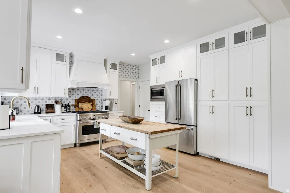 White shaker cabinetry, wood-finish flooring, stainless steel appliances, patterned tile backsplash, and a wood-top island with open shelving