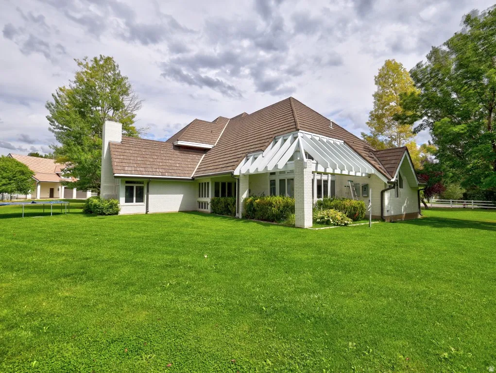 Expansive green lawn, white exterior siding, multi-gabled roofline, brick chimney, and an attached pergola structure
