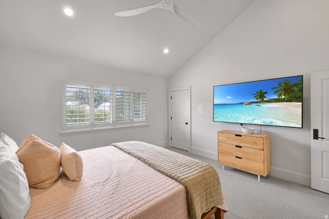 Vaulted ceiling with recessed lighting, white wood window shutters, light gray carpet flooring, and a ceiling fan