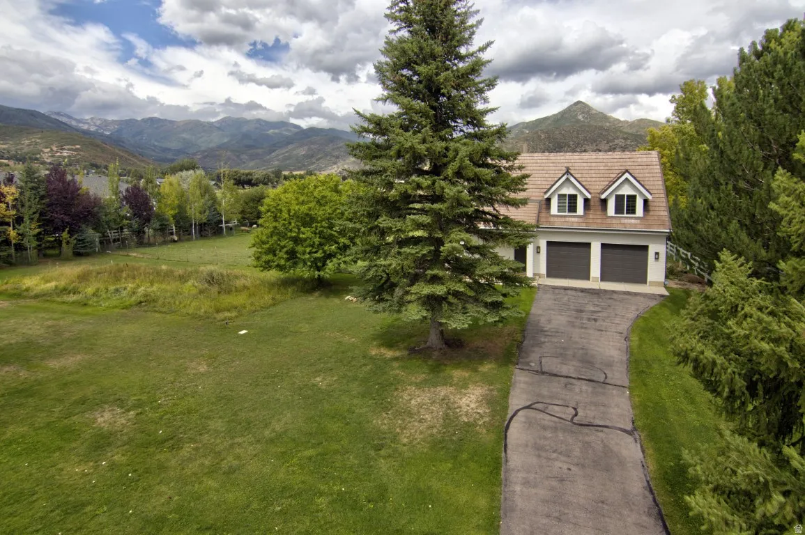 Property exterior with a two-car garage and dormer windows, situated on a grassy lot with mature trees