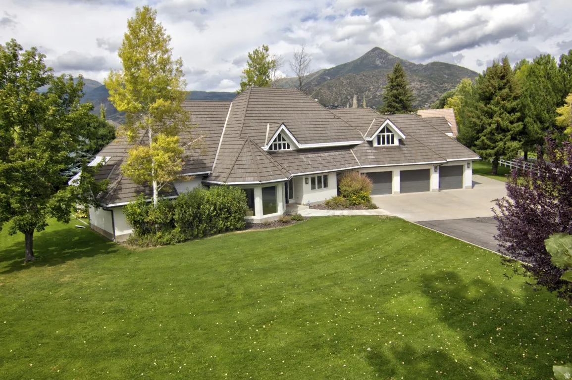 Expansive front lawn, mature trees, multi-car garage, dormer windows, mountain backdrop