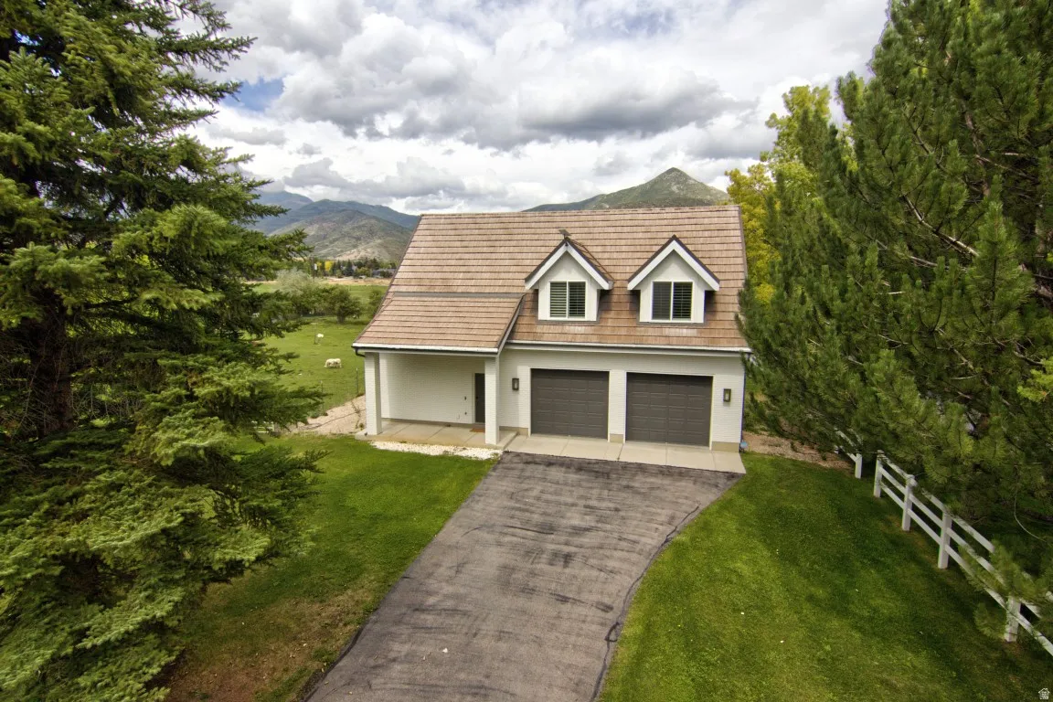 White exterior with a two-car garage, dormer windows, and a brown shingle roof