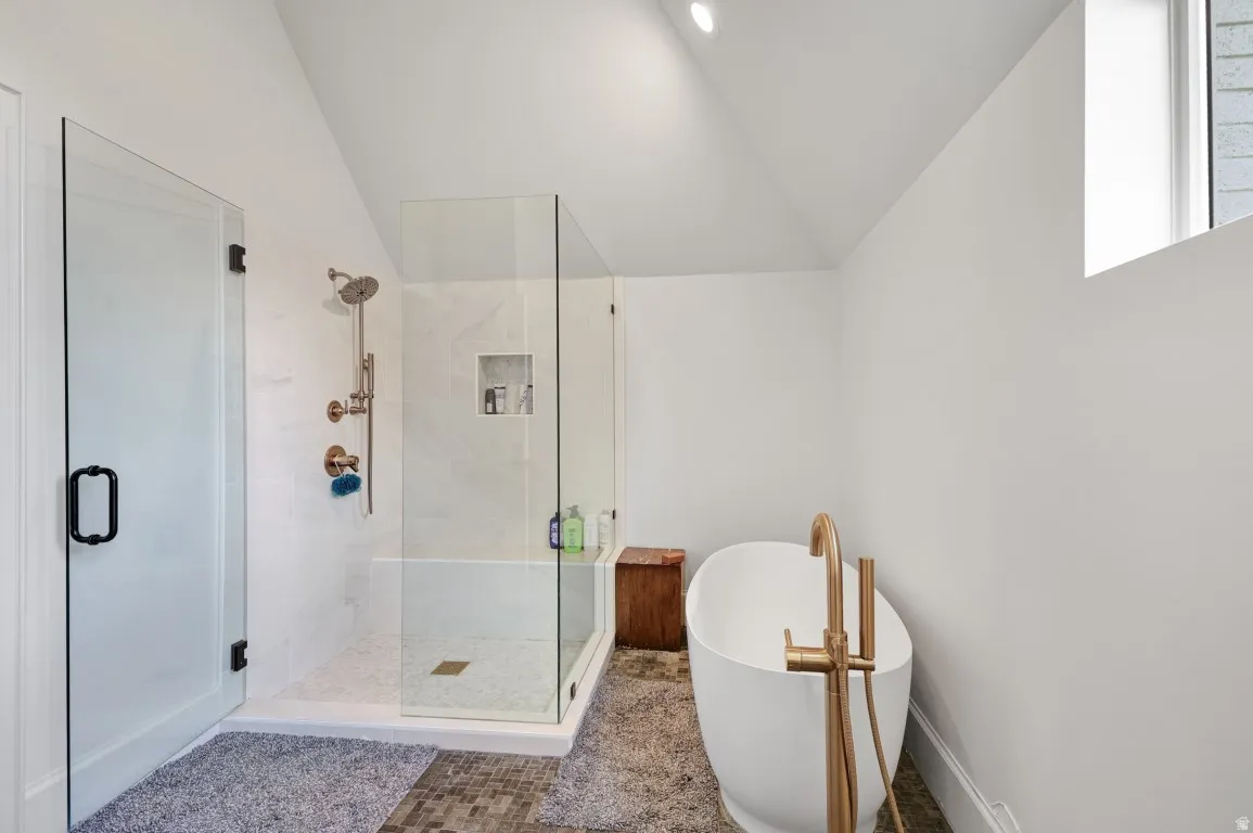 Freestanding soaking tub with a floor-mounted brass faucet, glass-enclosed shower with a rain shower head, and tile flooring