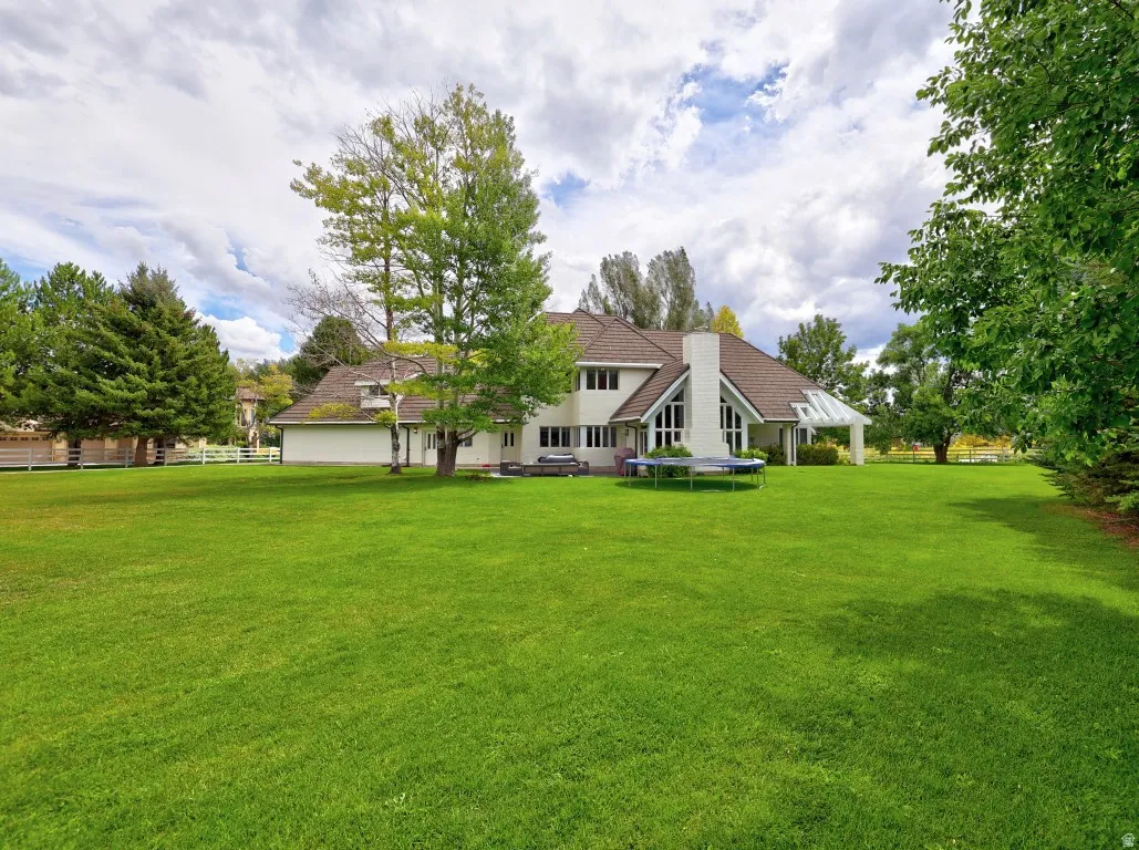 Expansive lawn with mature trees and a two-story residence featuring a prominent chimney and an attached covered patio