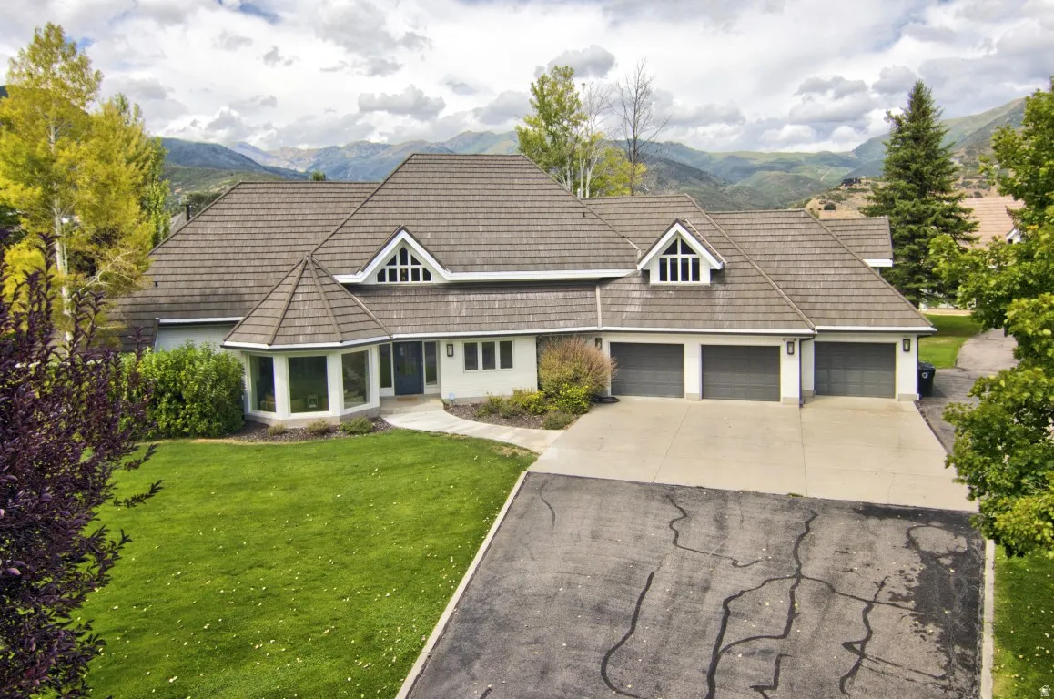 Multi-level residence featuring a prominent shingle roof, three garage bays, a turret-style bay window, and a concrete driveway