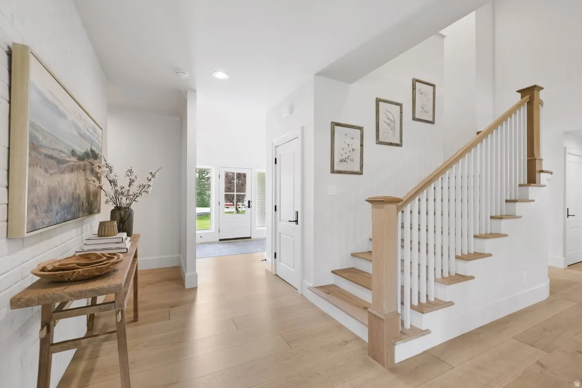 Hardwood flooring throughout, white brick accent wall, wood staircase with white balusters, recessed lighting, and a front entry door with glass panels