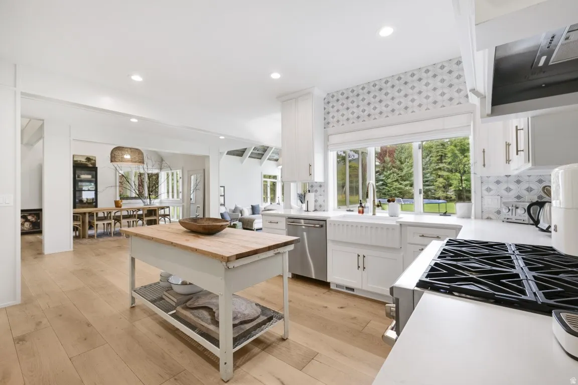 Kitchen featuring wood-finish flooring, white cabinetry, a farmhouse sink, stainless steel dishwasher, and a gas range