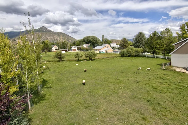 Expansive green space featuring a white picket fence and mature trees