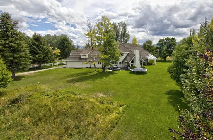 Expansive lawn with mature trees, a white picket fence, and a covered patio structure