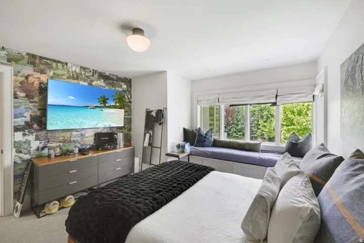 Built-in window seat with integrated storage, large window with natural scenery, wall-mounted television, and a ceiling-mounted light fixture