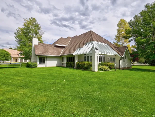 Expansive green lawn, white exterior siding, multi-gabled roofline, brick chimney, and an attached pergola structure