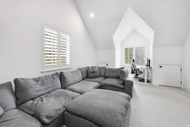 Vaulted ceiling, two windows with plantation shutters, recessed lighting, and light-toned carpeting