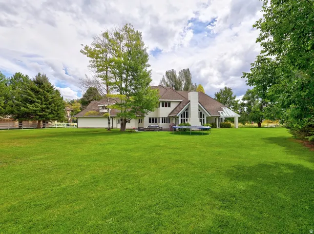 Expansive lawn with mature trees and a two-story residence featuring a prominent chimney and an attached covered patio
