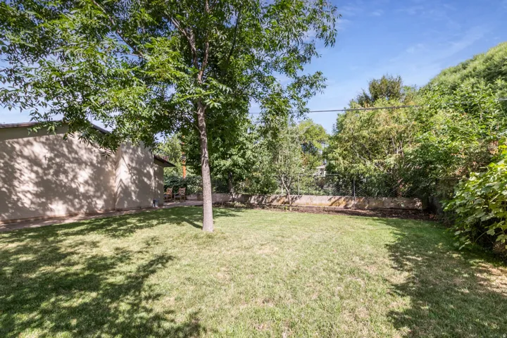 Expansive grassy yard with mature trees, a stucco exterior, and surrounding natural foliage