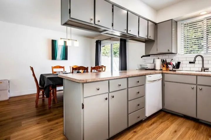 Kitchen featuring wood-finish flooring, shaker-style cabinetry, a built-in dishwasher, and a subway tile backsplash