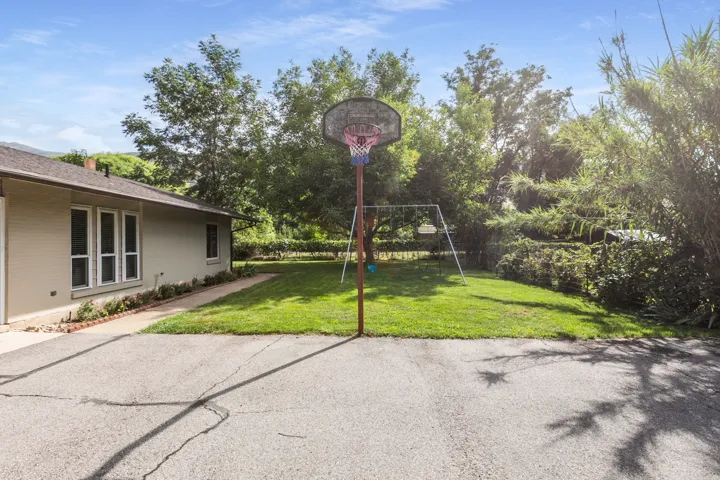 Expansive backyard featuring a green lawn, mature trees, and a basketball hoop