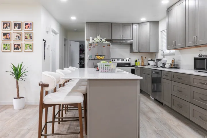 Kitchen featuring an island with countertop seating, stone countertops, gray cabinetry, stainless steel appliances, and wood-finish flooring