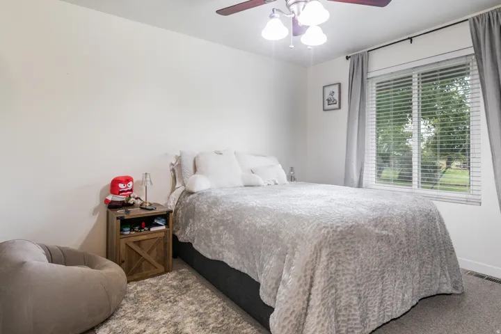 Spacious room featuring a ceiling fan with integrated lighting, a large window with blinds, and neutral wall tones