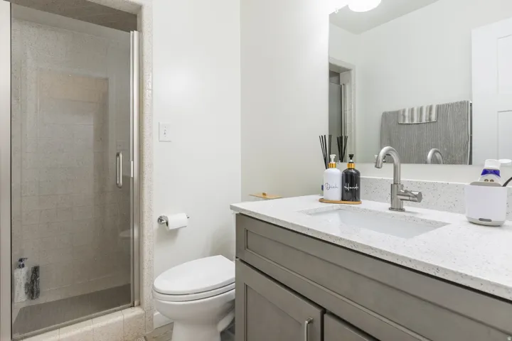 Shower with glass enclosure, white vanity with integrated sink, stone-finish countertop, brushed nickel faucet, and built-in cabinetry