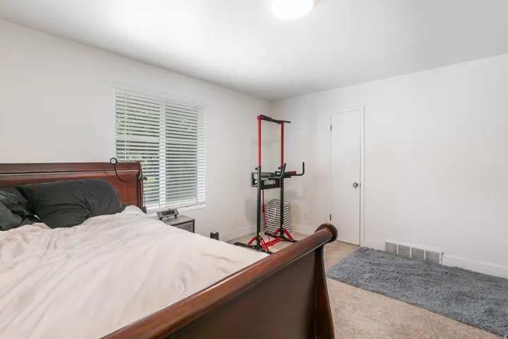 Spacious primary bedroom featuring a wood-finish bed frame, generous floor space, and abundant natural light from shuttered windows