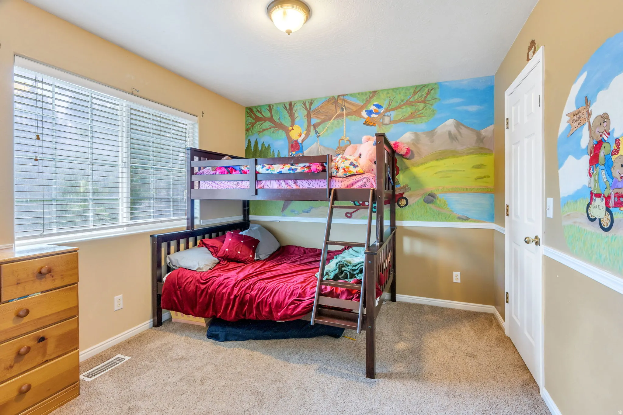 Wall-to-wall carpeting, window with blinds, overhead lighting, and painted wall decor