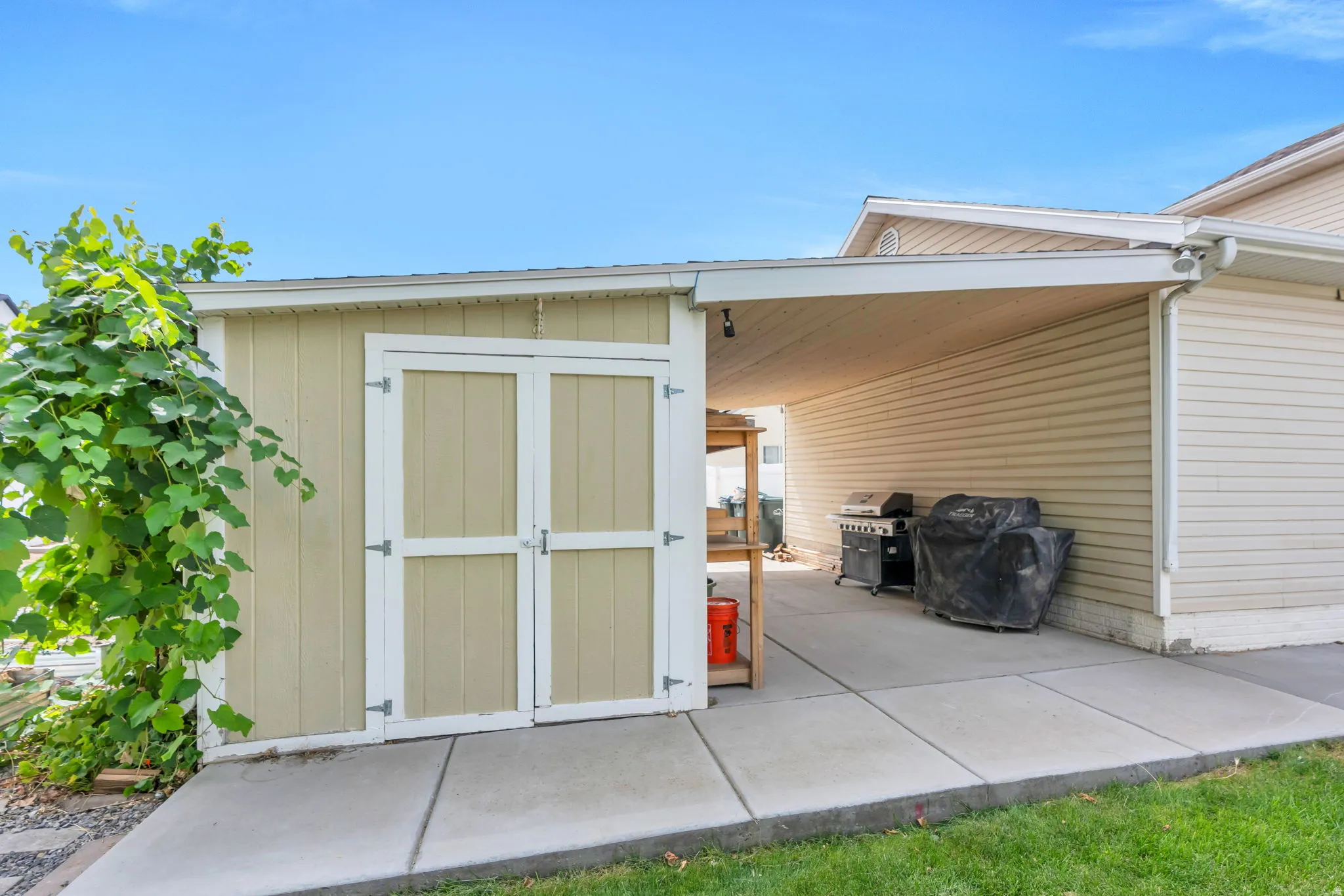 Attached storage shed with double doors, covered patio area, and concrete hardscaping
