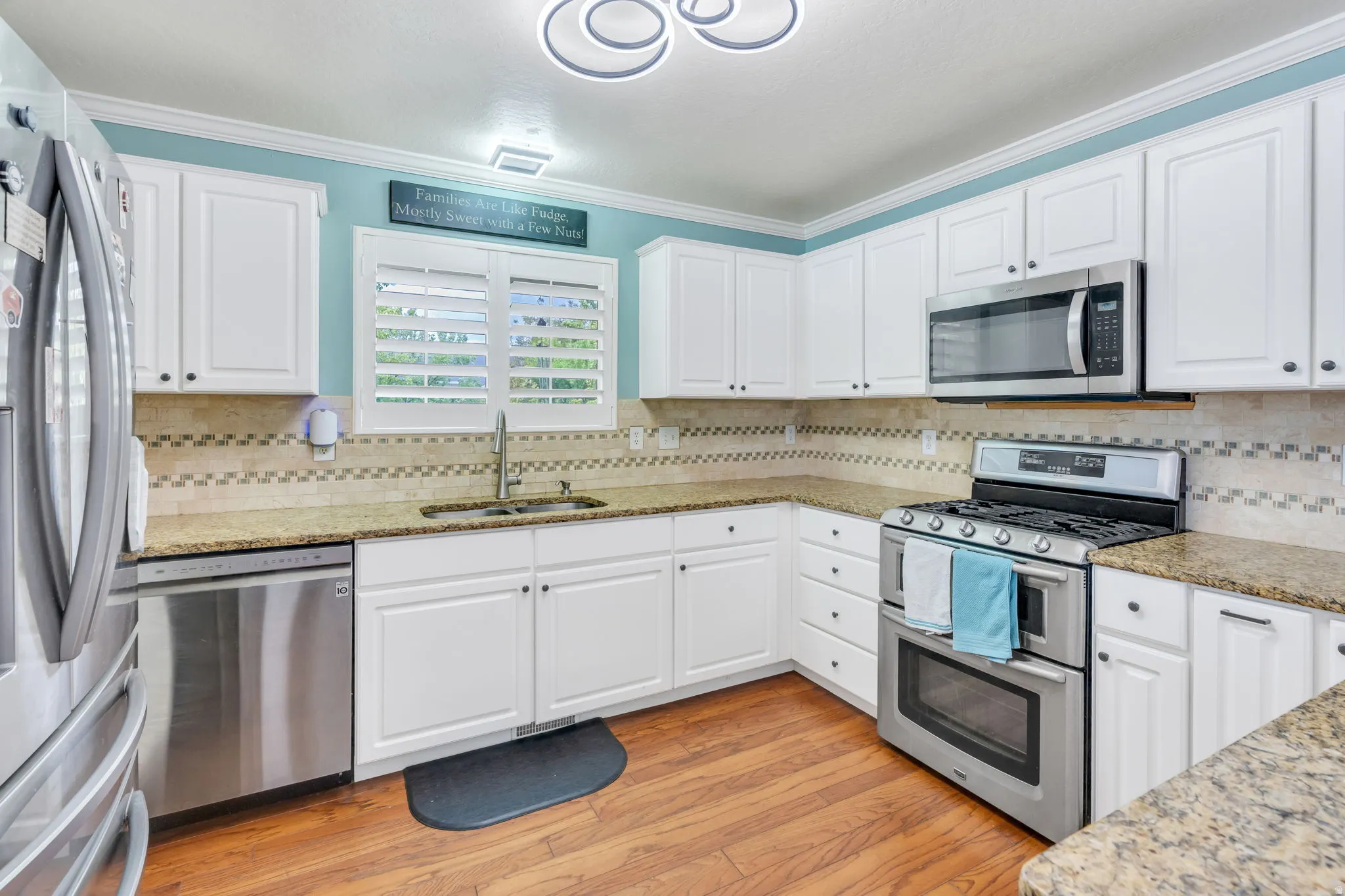 White cabinetry, granite-finish countertops, stainless steel appliances, wood-finish flooring, and a patterned tile backsplash