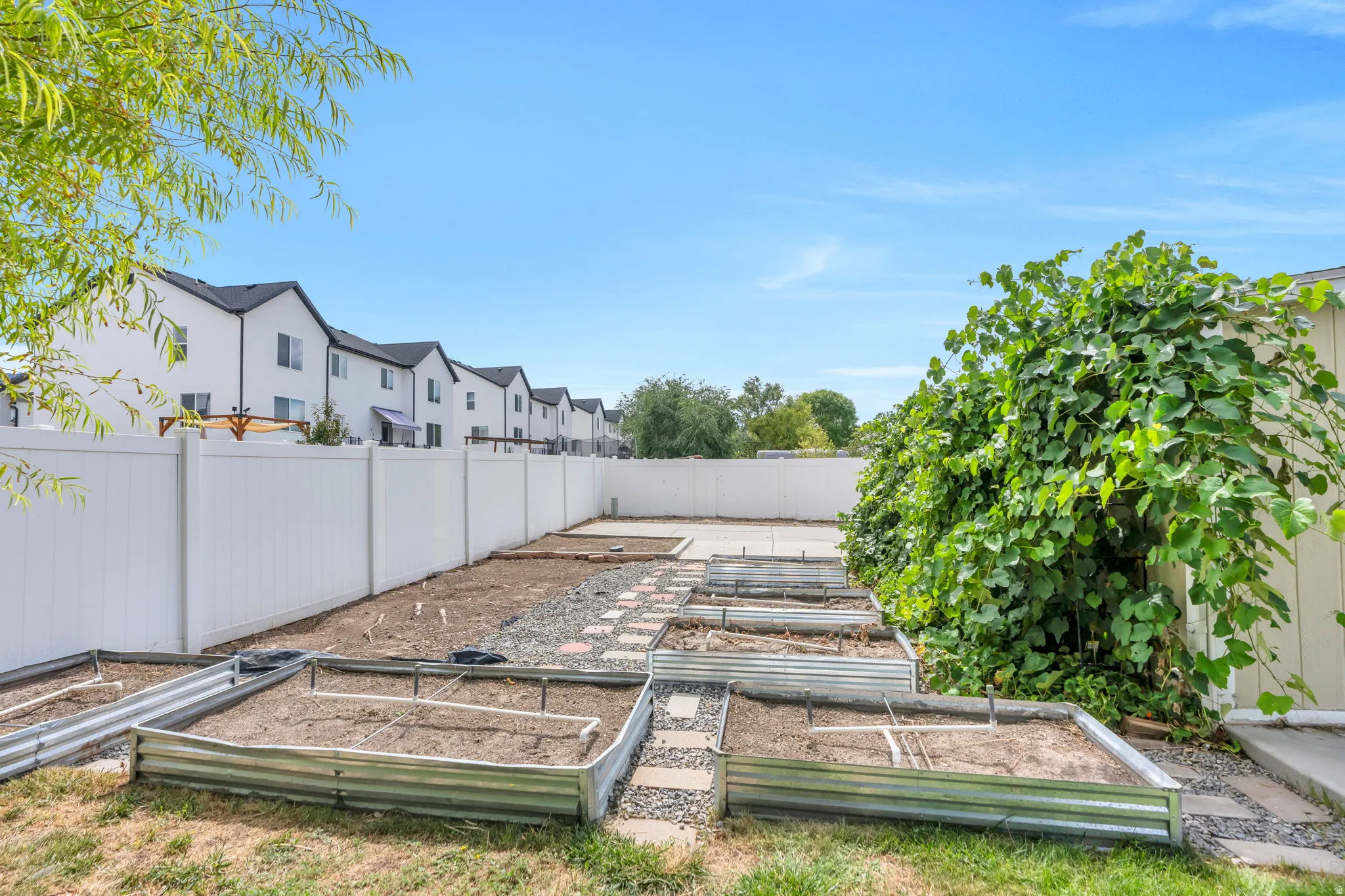 Private backyard featuring a white vinyl fence, multiple raised garden beds, and a paved patio area