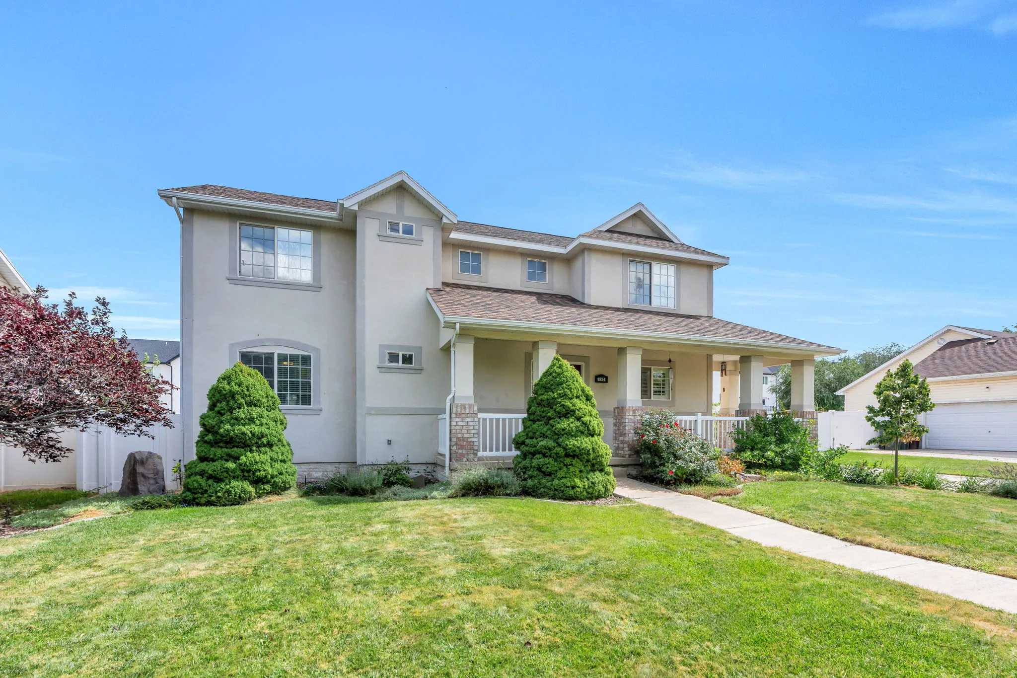 Two-story stucco exterior with gabled roof lines, covered front porch, and mature front yard landscaping