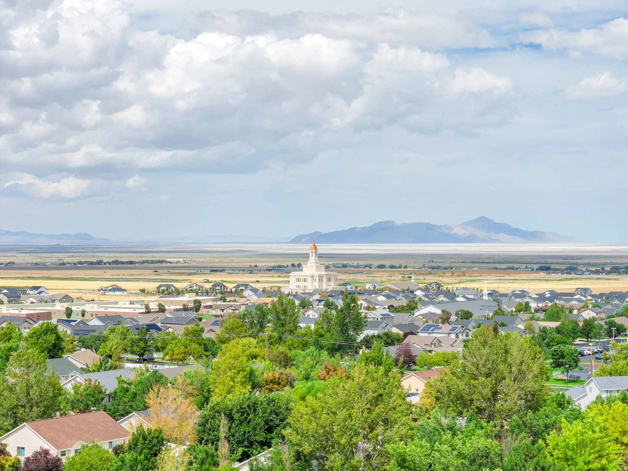 Expansive aerial showing residential area, distant mountains, and a prominent building with a red-domed cupola